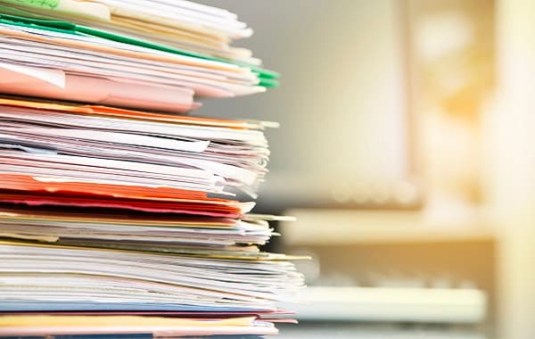 Large stack of files, documents, paperwork on desk.